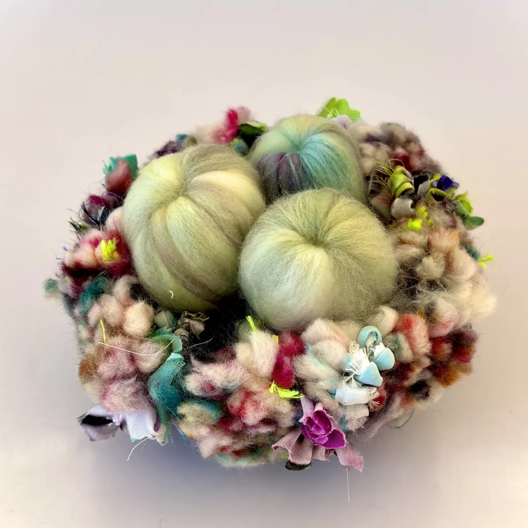 Fragment P-002 — 10 × 10 cm — 2026
Tufted wool, cotton, carded wool, silk ribbons.
An isolated textile nest, sheltering several latent floral forms. Fragment from a larger structure, where the bird does not protect its eggs but cultivates floral forms it feeds on.